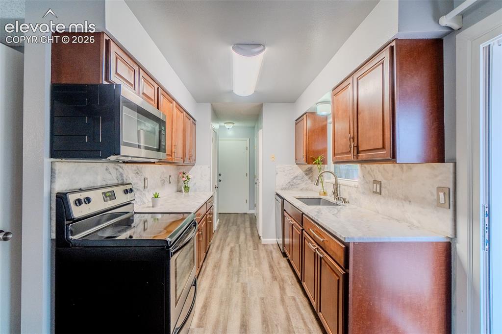 Image 12 of 33: Galley kitchen featuring wood-finish cabinetry, light-toned stone counterto