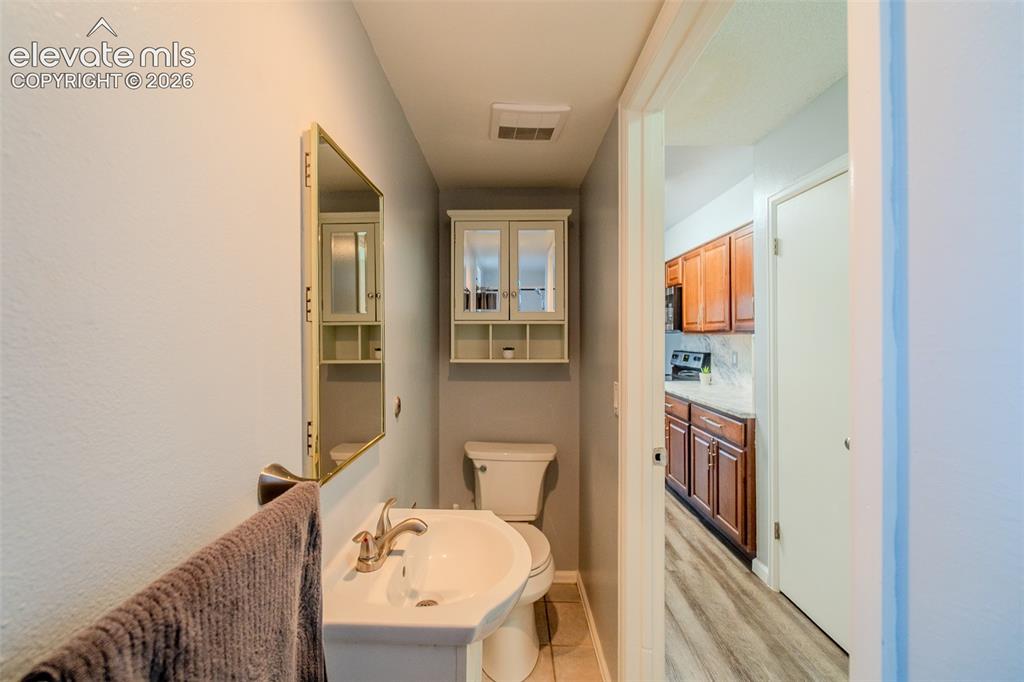 Image 13 of 33: Hallway powder room down the hall, featuring a pedestal sink, gold mirror, 
