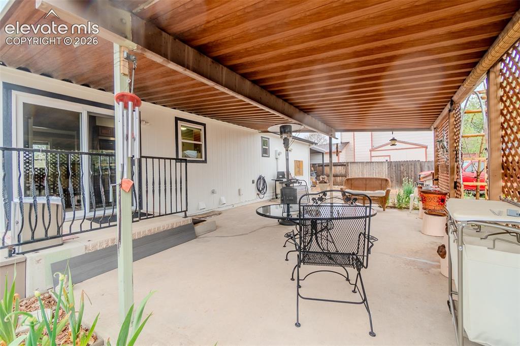 Image 28 of 33: Covered concrete patio featuring a wood-finish ceiling, lattice privacy scr