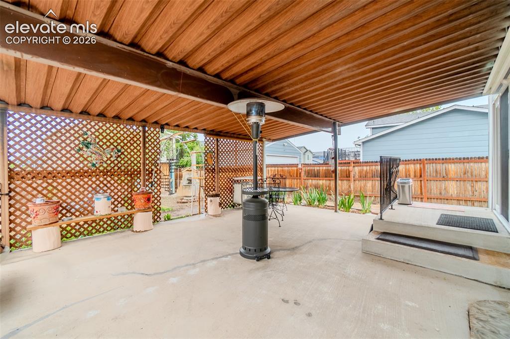Image 30 of 33: Concrete patio featuring a wood-finish slatted overhead cover and lattice-s