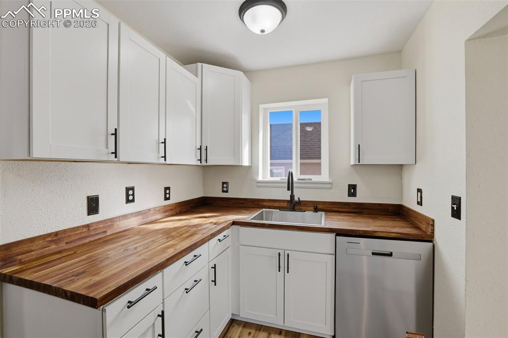 Image 10 of 36: Kitchen featuring butcher block countertops, dishwasher, white cabinets, an