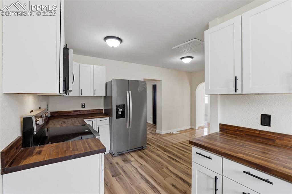 Image 11 of 36: Kitchen with butcher block counters, stainless steel appliances, white cabi