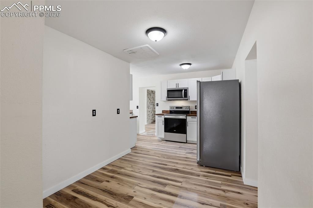 Image 8 of 36: Kitchen with stainless steel appliances, white cabinetry, and light wood-st