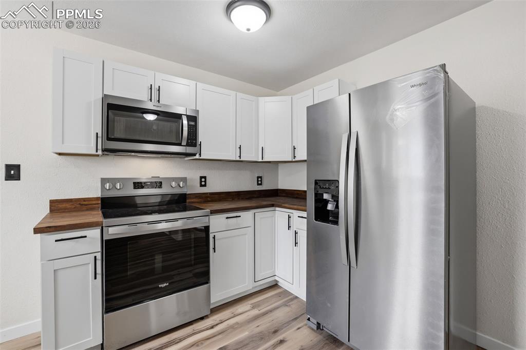 Image 9 of 36: Kitchen featuring stainless steel appliances, white cabinets, light wood-ty