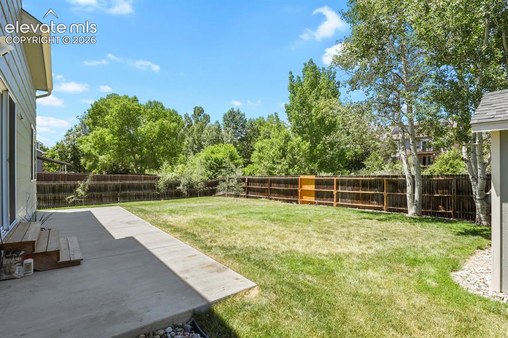 Image 32 of 46: Expansive backyard featuring a concrete patio, mature trees, a wooden fence