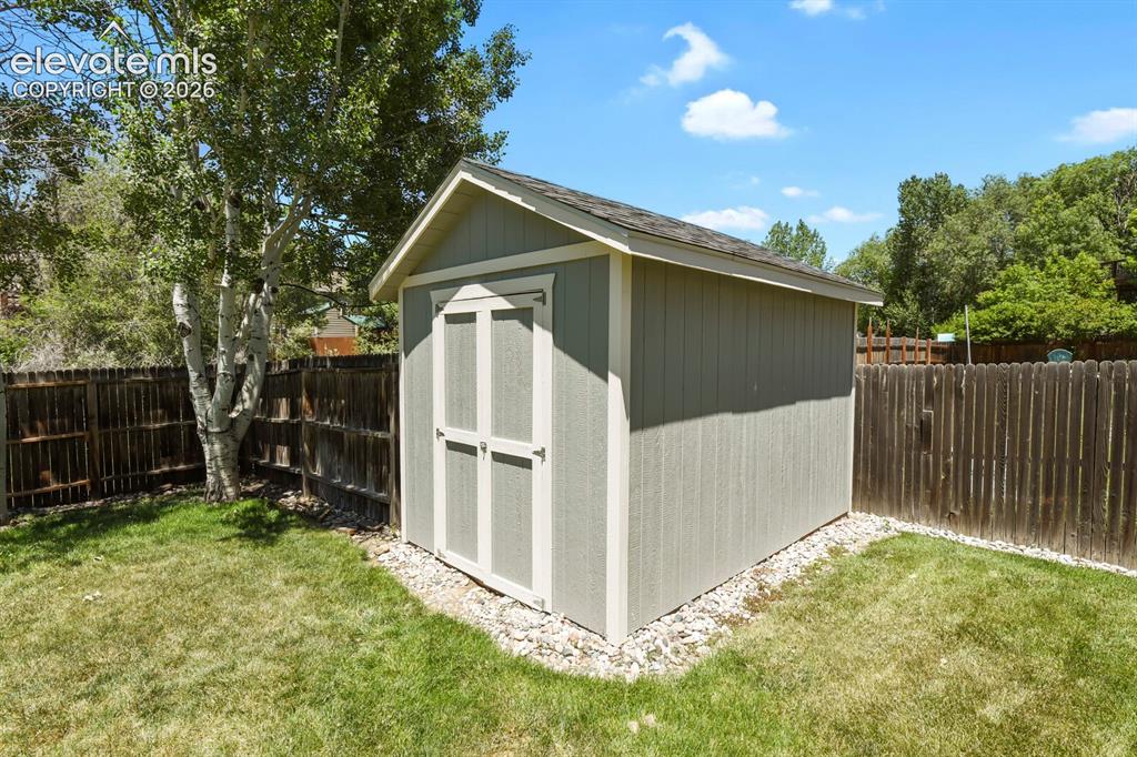 Image 36 of 46: Exterior storage shed with a gabled roof, light gray siding, and white trim