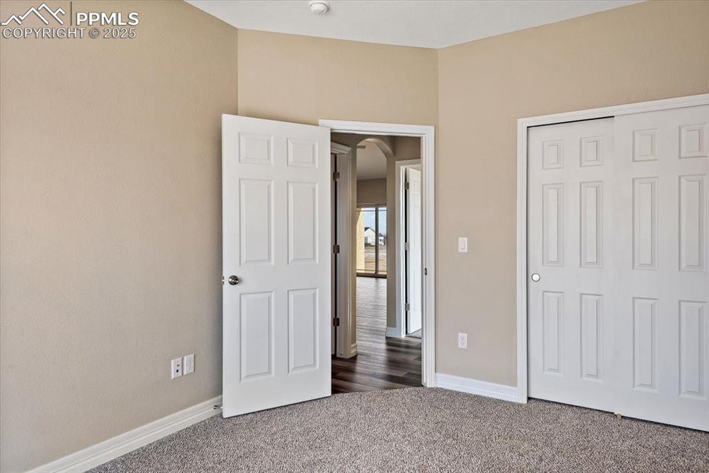Image 22 of 45: Unfurnished bedroom with arched walkways, baseboards, dark colored carpet,