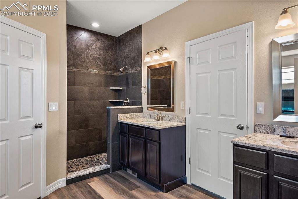 Image 26 of 45: Bathroom featuring a walk in shower, two vanities, a sink, and wood finishe