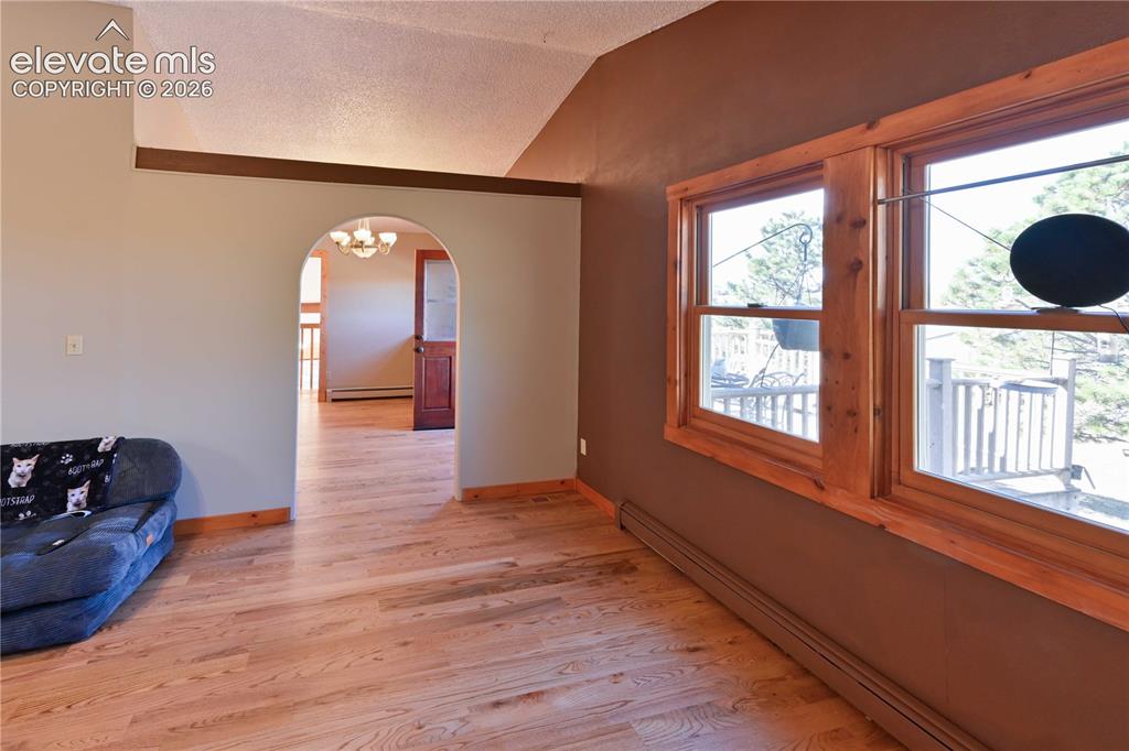 Image 13 of 40: Wood-finish flooring with natural wood trim, arched doorway, and vaulted ce