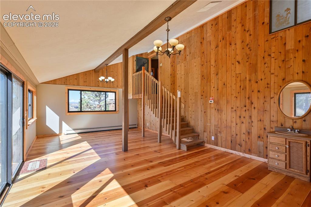 Image 25 of 40: Vaulted ceiling with exposed wood beam, wood-paneled accent wall, hardwood 