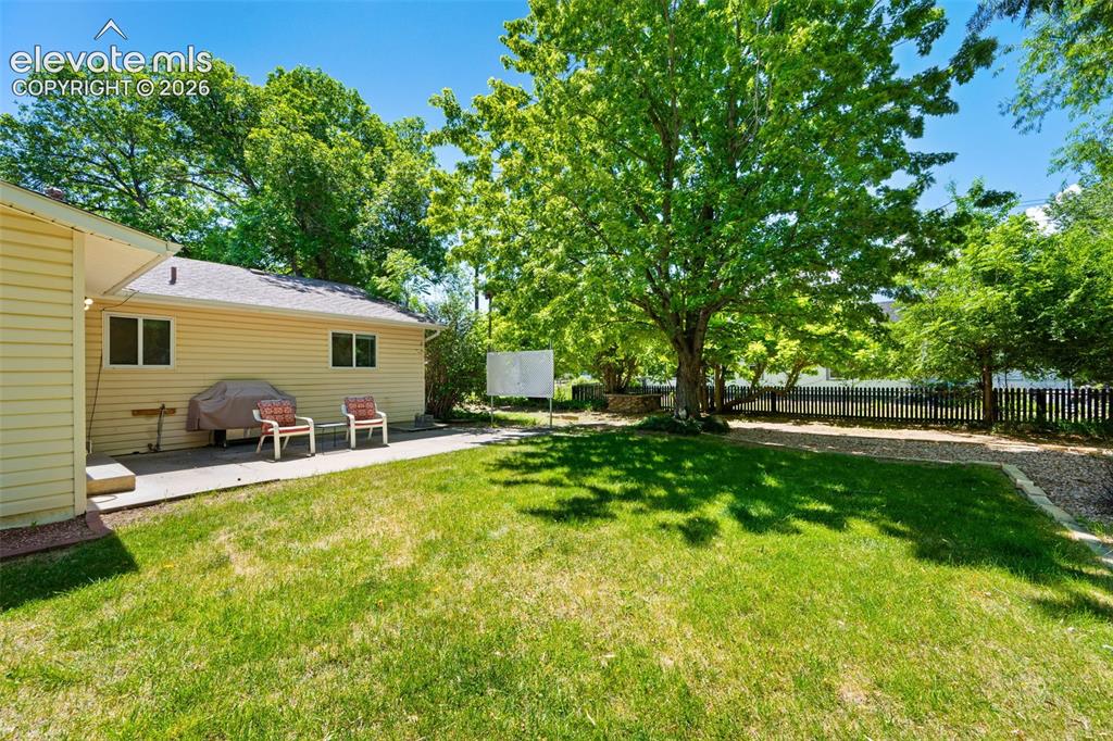 Image 27 of 36: Spacious backyard featuring a large concrete patio, manicured lawn, and mat