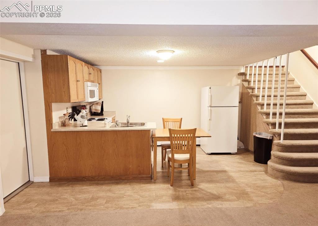 Image 17 of 39: Stairs to basement. Second kitchen with light countertops, white appliances
