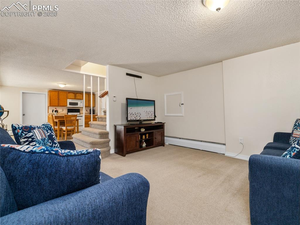 Image 20 of 39: Living area with stairway, light carpet, a baseboard heating unit, and a te