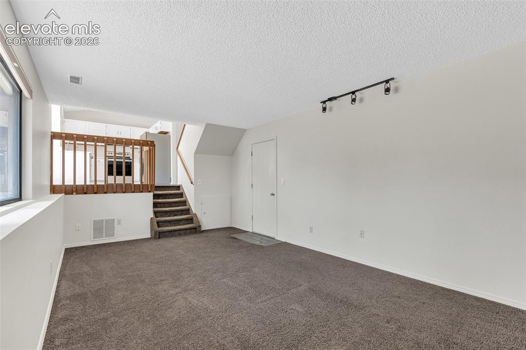 Image 26 of 33: Neutral tone carpeting with white walls, track lighting, and a window