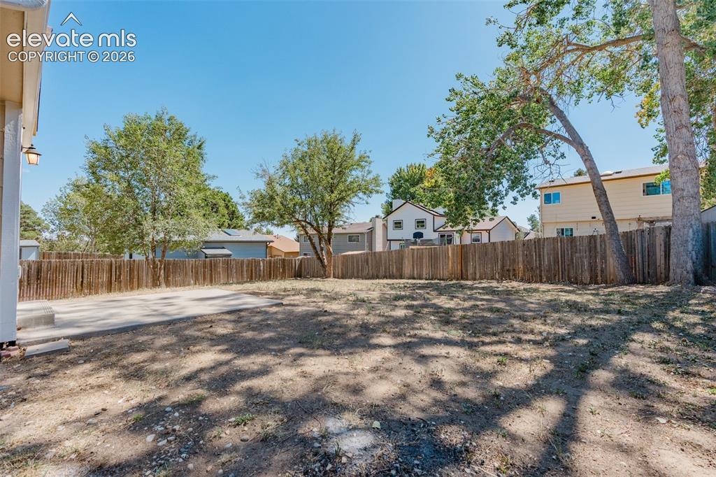 Image 28 of 33: Expansive backyard with a full privacy fence, concrete patio, and mature tr