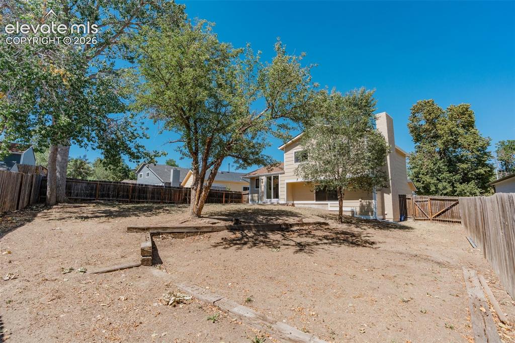 Image 30 of 33: Expansive fenced backyard with mature trees, a two-story exterior, and a bu
