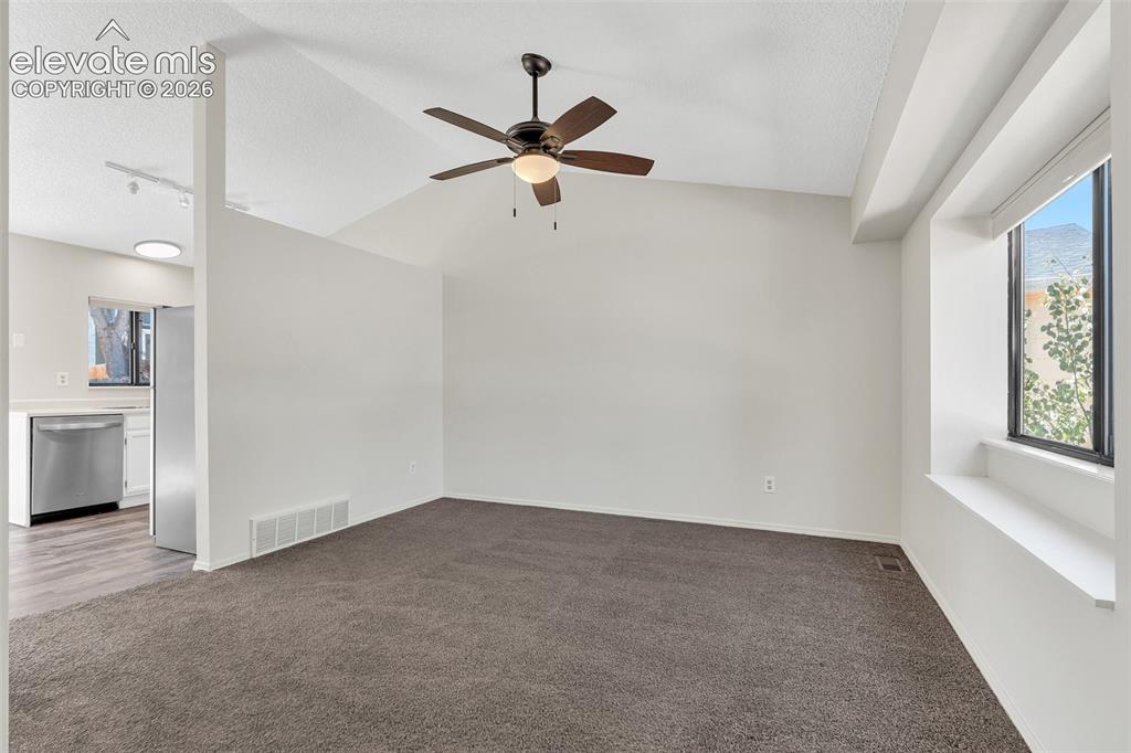 Image 4 of 33: Vaulted ceiling with a ceiling fan, carpeted flooring, and a large window w