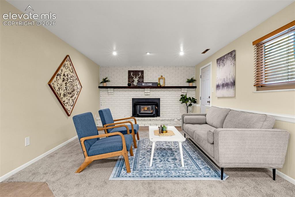 Image 21 of 38: Living area featuring a white brick fireplace with a dark wood mantel, rece