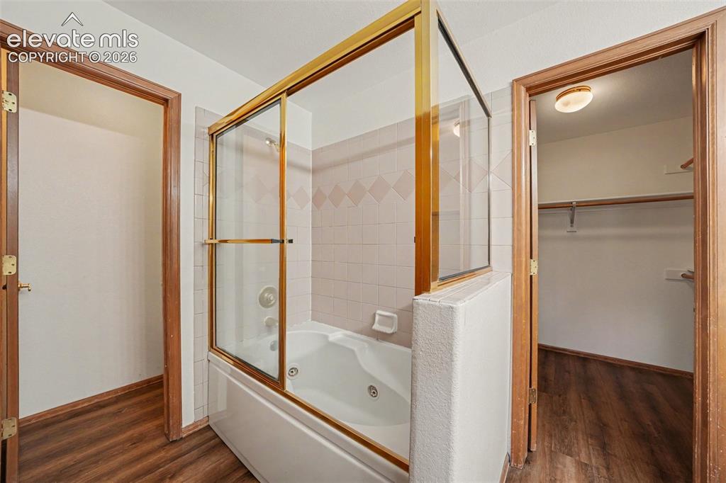 Image 24 of 47: Jetted tub with gold-finish sliding glass enclosure, white tile surround, a