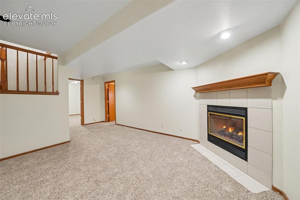 Image 33 of 47: Carpeted living space with a tile-surround fireplace featuring a wood mante