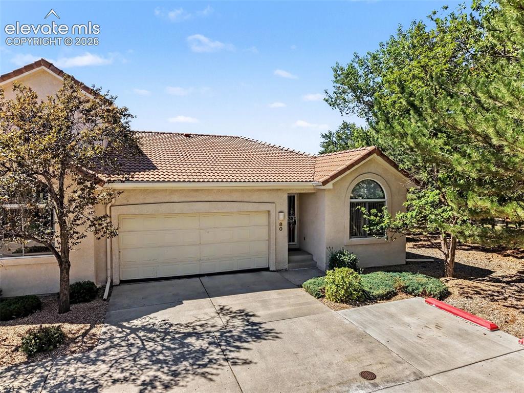 Image 44 of 47: Stucco exterior featuring a tile roof, an arched window, and an attached ga