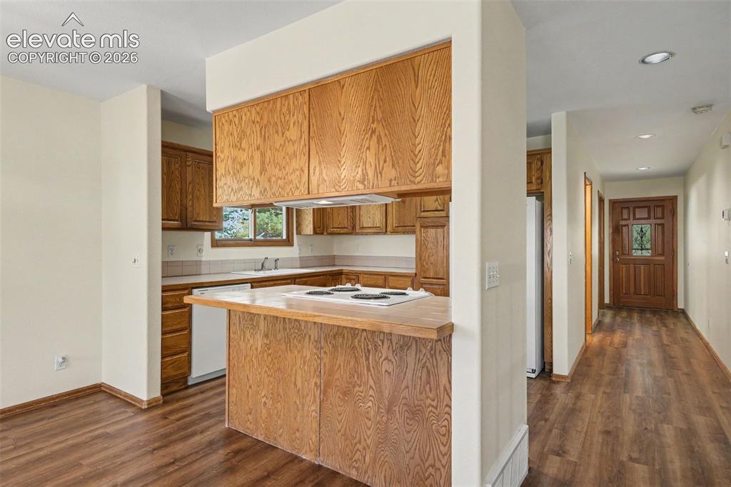 Image 9 of 47: Kitchen featuring wood cabinetry, white appliances, and a breakfast bar