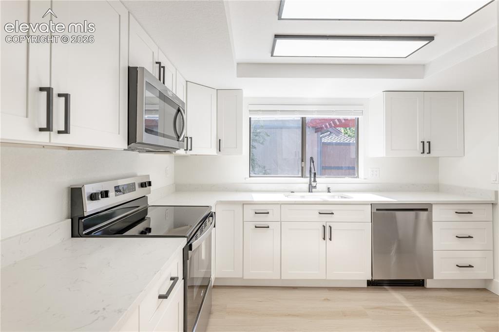 Image 10 of 28: Kitchen featuring white shaker-style cabinetry, quartz countertops, stainle