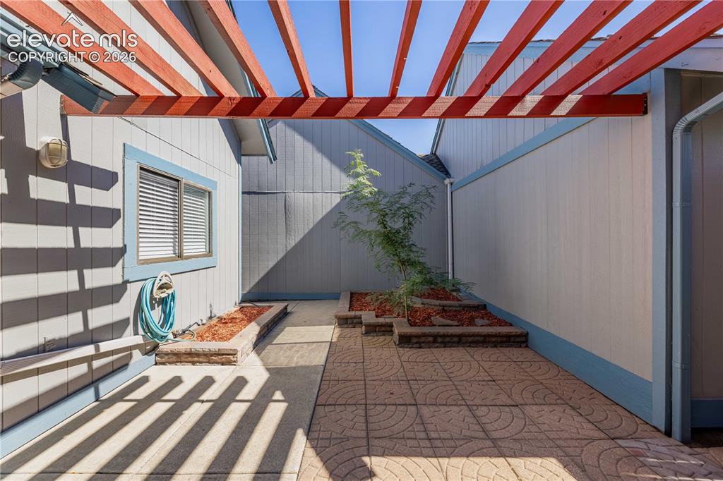 Image 18 of 28: Private courtyard featuring a wood-beam pergola, stamped concrete patio, an