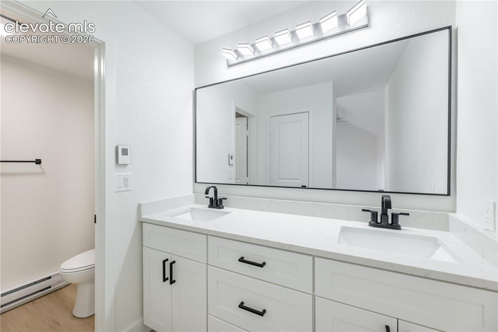 Image 22 of 28: Dual-sink vanity featuring a stone countertop, white shaker-style cabinetry