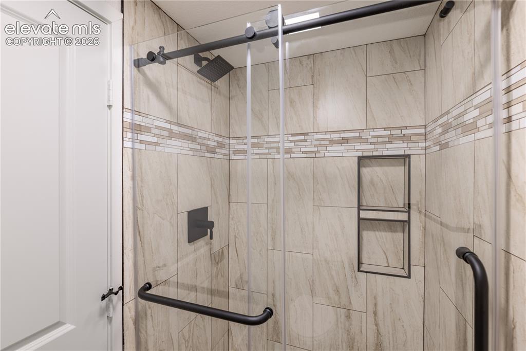 Image 23 of 28: Walk-in shower featuring large-format stone-finish wall tile, decorative ho
