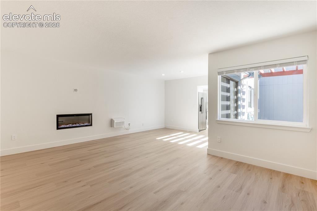 Image 3 of 28: Open living area featuring wood-finish flooring, a wall-mounted electric fi