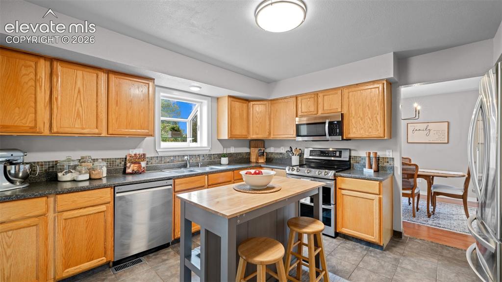 Image 10 of 30: Kitchen featuring wood cabinetry, stainless steel appliances, dark countert