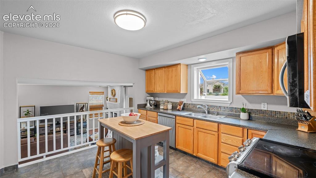 Image 12 of 30: Kitchen featuring wood cabinetry, dark countertops, and a tiled backsplash