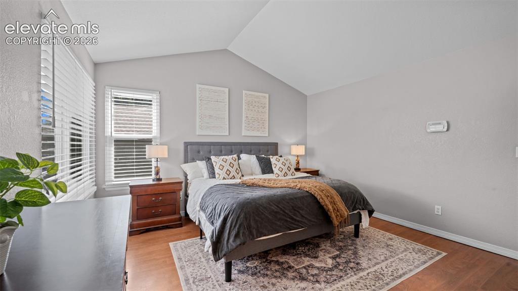 Image 23 of 30: Vaulted ceiling bedroom featuring wood-finish flooring and two white-trimme