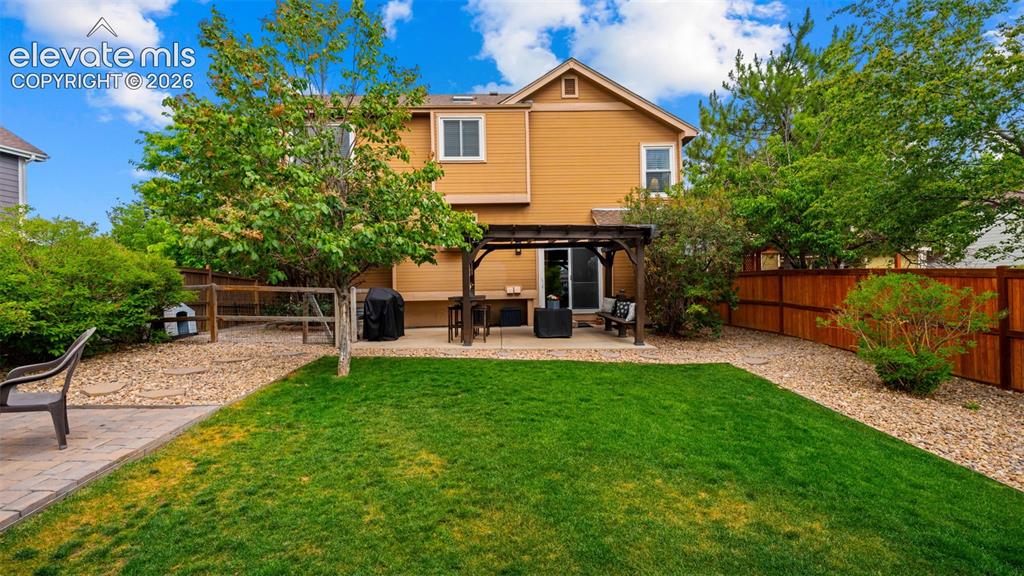 Image 27 of 30: Expansive rear yard featuring a green lawn, paved patio, and pergola