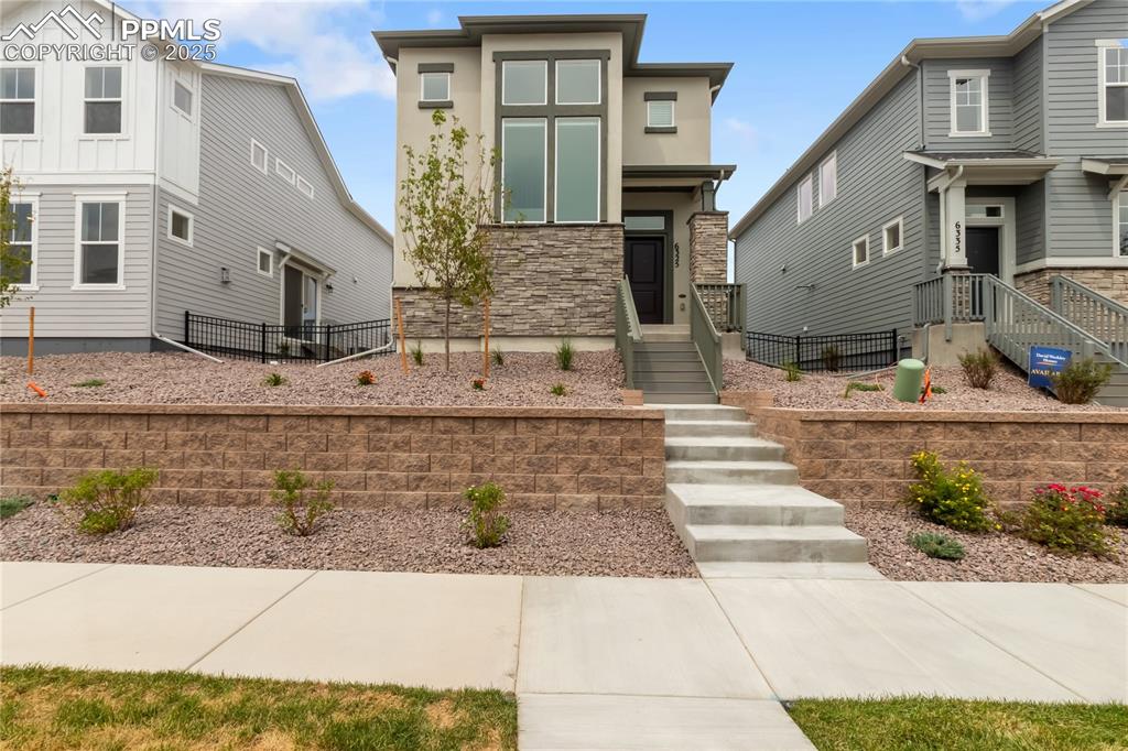 Caption: View of front of house with stone siding and stucco siding