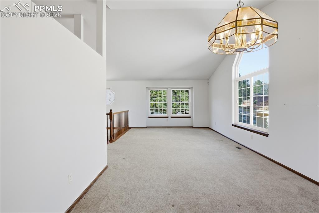 Image 15 of 47: Spare room with carpet, a chandelier, and high vaulted ceiling