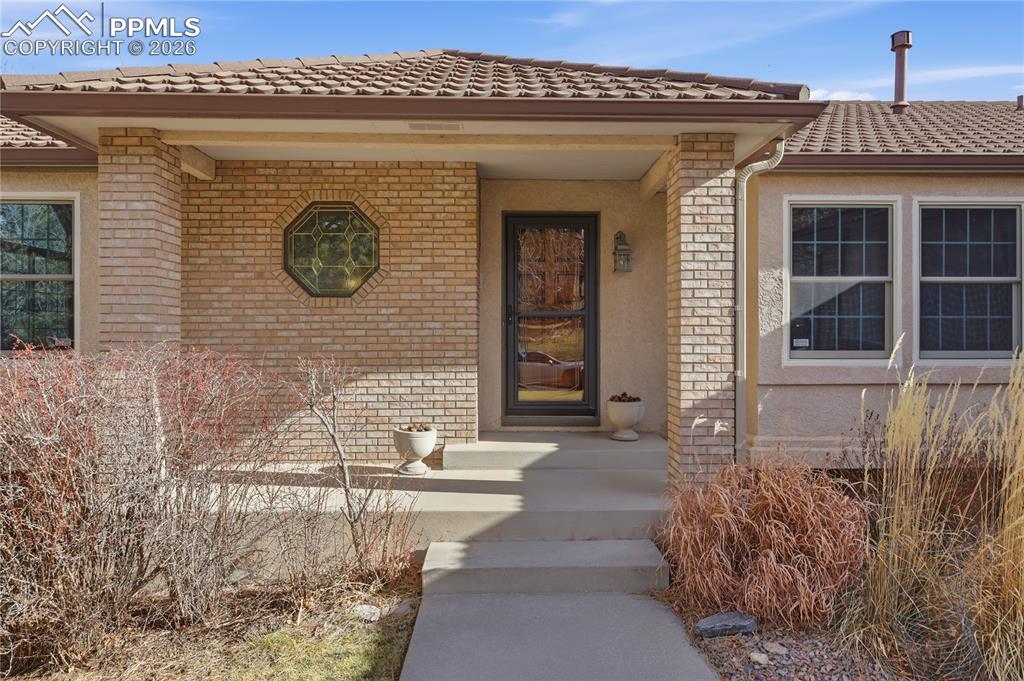 Image 4 of 47: Doorway to property featuring brick siding, a tile roof, and stucco siding