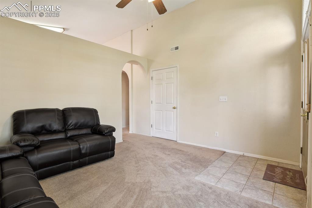 Image 9 of 29: Living room with high vaulted ceiling, ceiling fan, and light carpet