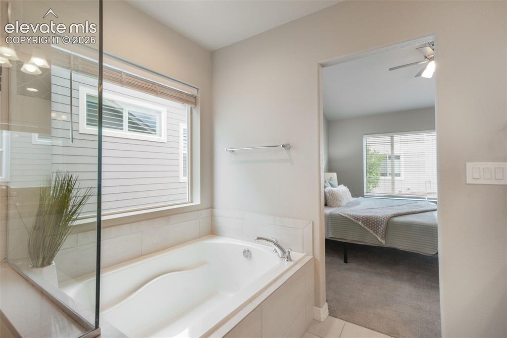 Image 28 of 49: Soaking tub with tile surround, framed by a large window