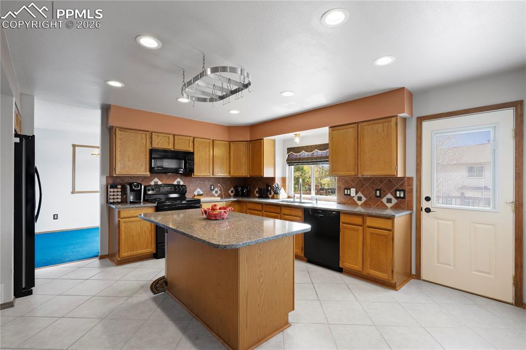 Image 10 of 46: The kitchen features wood cabinetry, black appliances, a central island wit