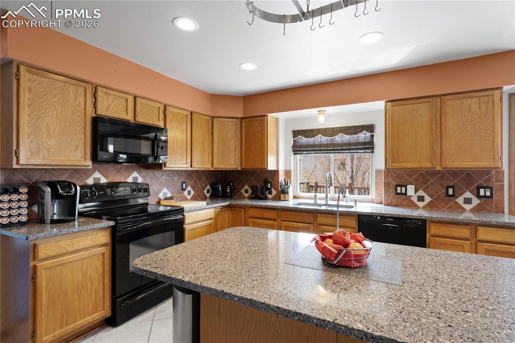 Image 11 of 46: Well-appointed kitchen featuring wood cabinetry, black appliances, speckled
