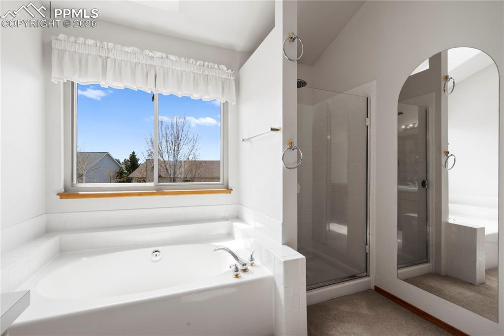 Image 22 of 46: This bathroom features a garden tub below a window, a glass-enclosed shower