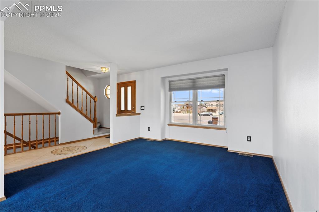 Image 4 of 46: The living area features carpet, white walls, and a large window with blind