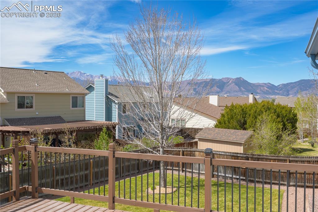 Image 42 of 46: Outdoor deck with wood railings and metal balusters overlooking a fenced ya
