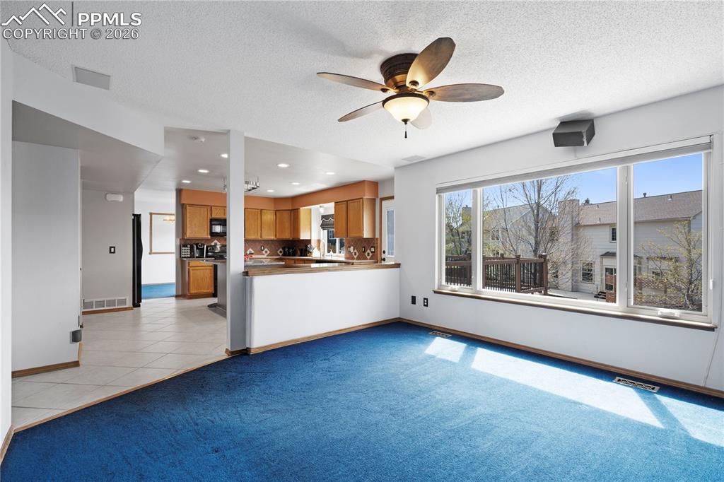 Image 9 of 46: Living area featuring blue carpeting, a ceiling fan with light fixture, and
