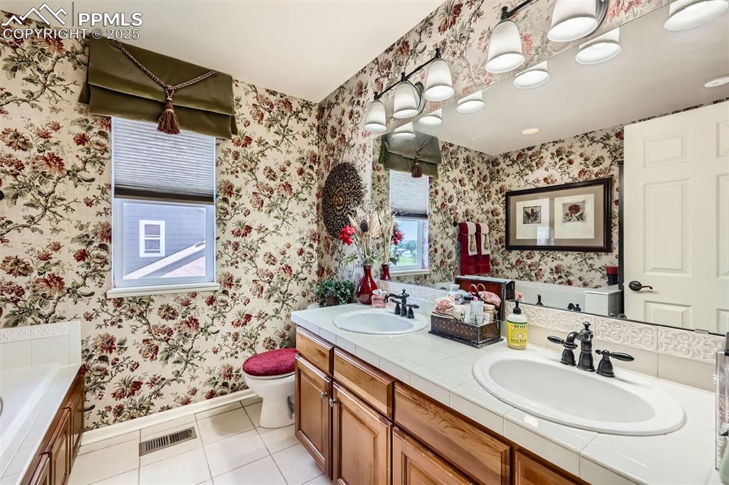 Image 18 of 30: Bathroom featuring wallpapered walls, tile patterned flooring, double vanit