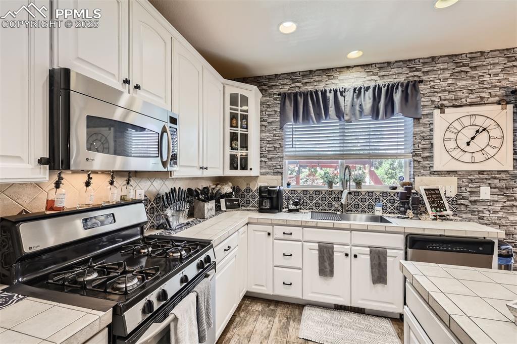 Image 8 of 30: Kitchen with appliances with stainless steel finishes, tile counters, glass