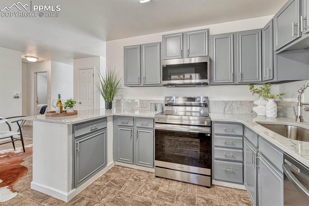 Image 13 of 43: Kitchen featuring gray cabinetry, a peninsula, stainless steel appliances, 