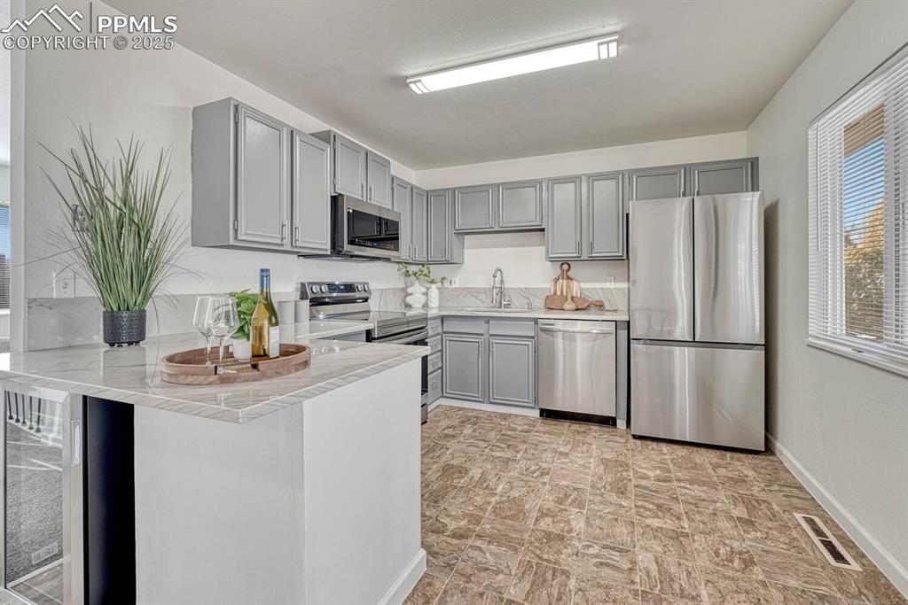 Image 14 of 43: Kitchen featuring gray cabinets, appliances with stainless steel finishes, 